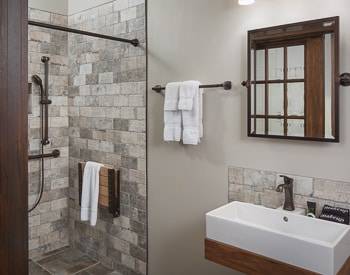 Square grey stone Shower with the stone continuing on the bathroom floor. Floating white sink outlined in wood